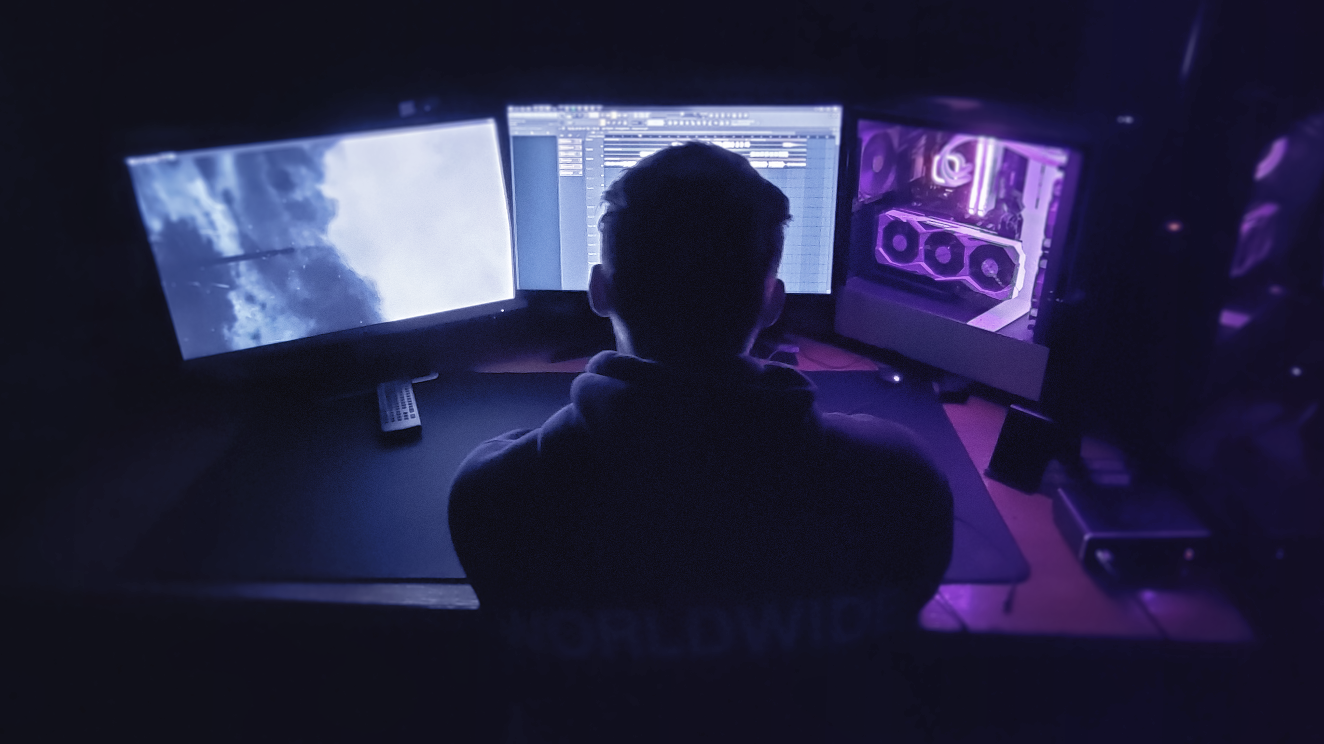 PEG working at a desk with two large screens and a purple LED-lit PC case